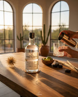 Botella de Sotol Cara Blanca Ultra Premium 750ml sobre mesa de madera, con vaso y coctelera. Licomar, Vinos y Licores.